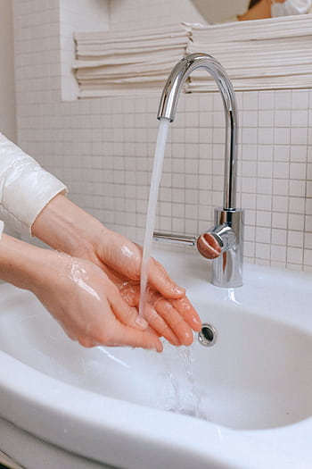 Close-up of hands being washed under running water in a bathroom sink for hygiene and virus prevention. HD phone wallpaper