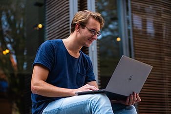 A young man sitting outdoors in Leiden, Netherlands, working on a laptop. HD wallpaper