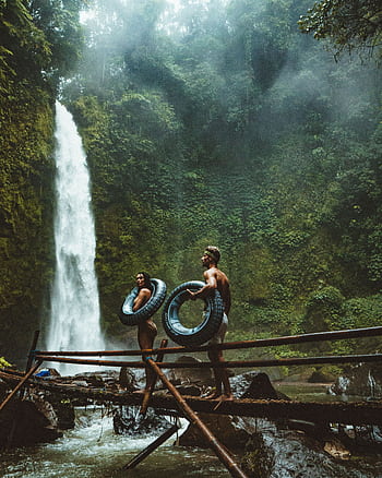 A couple in swimwear with float tubes exploring a lush waterfall in Bali, Indonesia. HD phone wallpaper
