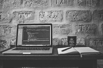 Black and white of a coding workspace with a laptop, mug, and notebook. HD wallpaper