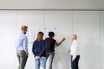 A diverse team of professionals engaged in strategic planning using a whiteboard in an office setting. HD wallpaper
