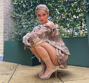 Addison Rae, green work in progress barriers, crouching down, short dress, brunette, trees, jewelry, roman style heels HD wallpaper