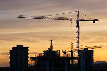 Silhouette of construction cranes and buildings against a vibrant sunset urban skyline. HD wallpaper