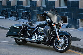 Classic black motorcycle parked beside a building in the city, showcasing its vintage design. HD wallpaper