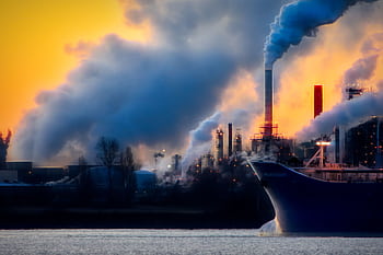 A factory emits thick smoke and pollution against a vibrant sunset, highlighting industrial impact on the environment. HD wallpaper