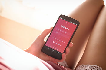 Woman holding a smart with Instagram login screen while relaxing indoors. HD wallpaper