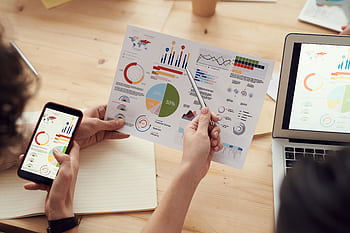 Team members analyze charts during a business meeting with laptops and smarts. HD wallpaper