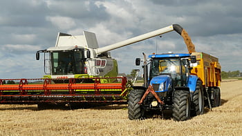 A modern combine harvester and tractor working together to harvest wheat in a sunny outdoor field. HD wallpaper