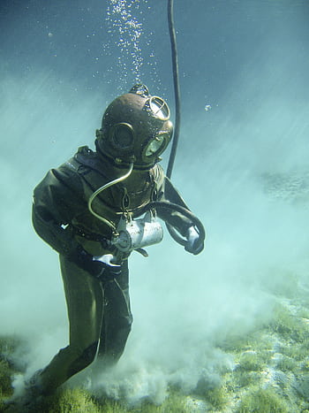 A vintage diver in a classic suit explores underwater, surrounded by clouds of sand. HD phone wallpaper