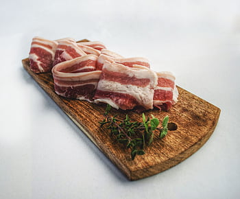 Sliced bacon laid on a rustic wooden board with herbs, showcasing a delicious and inviting food presentation. HD wallpaper