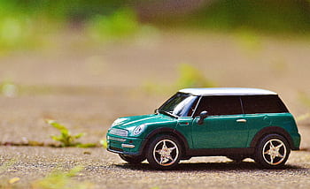 Green toy Mini Cooper car on pavement featuring a shallow depth of field outdoors. HD wallpaper
