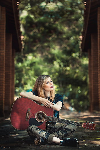 Woman sitting with guitar in an outdoor setting, exuding a relaxed vibe. HD phone wallpaper