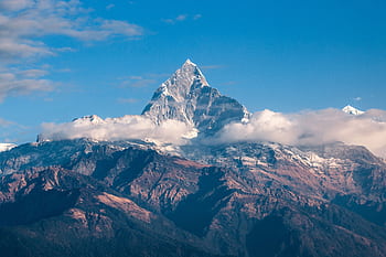 Breathtaking view of a snow-covered mountain peak surrounded by clouds during sunrise. HD wallpaper
