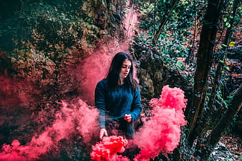 A woman stands in a forest with vibrant red smoke surrounding her, creating a mystical atmosphere. HD wallpaper