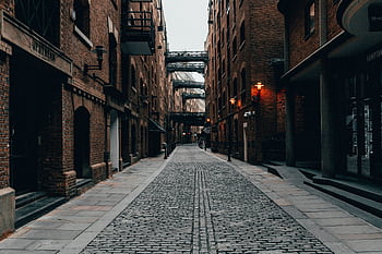 Cobblestone alleyway in London's atmospheric downtown, enclosed by brick buildings. HD wallpaper