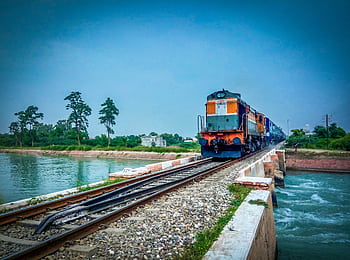 A train travels over a bridge spanning a serene river in a lush landscape. HD wallpaper