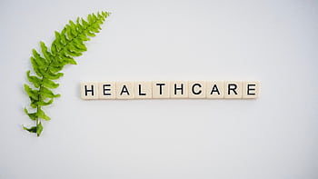 Healthcare word spelled with Scrabble tiles next to a green fern leaf on a white background. HD wallpaper