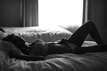 Artistic silhouette of a woman in lingerie reclining on a bed in muted lighting. HD wallpaper