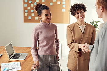 Business colleagues in an office shaking hands and smiling, showcasing teamwork and collaboration. HD wallpaper