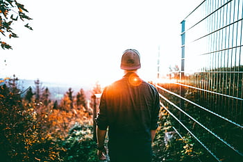 A man in casual wear walks through an idyllic forest at sunset, capturing a tranquil moment. HD wallpaper