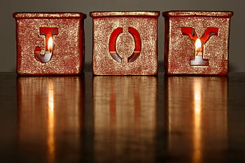 Three candlelit blocks spelling 'JOY' with a glowing warm reflection on a wooden table. HD wallpaper