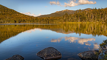 Stones On Water Lake Surrounded By Trees Forest Mountains Background Under Blue Sky Reflection On Water Nature HD wallpaper