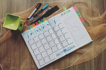 Top view of a January planner with pens and a green cup, ideal for organizing tasks. HD wallpaper