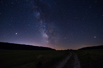 A stunning view of the Milky Way dominating the night sky over a serene open field pathway. HD wallpaper