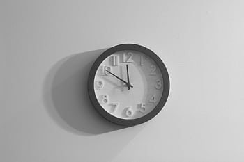 A black and white wall clock casting a shadow against a plain wall. HD wallpaper