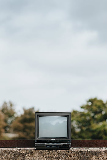 A vintage TV sits on a concrete wall outdoors with trees blurred in the background. HD phone wallpaper