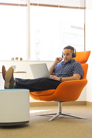 A man relaxes while working remotely in a modern office with a laptop and heads. HD phone wallpaper