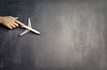 A hand holding a toy airplane on a blank blackboard symbolizes travel, exploration, and creative plans. HD wallpaper