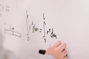 Person writing math equations on a whiteboard, focusing on integrals and formulas. HD wallpaper