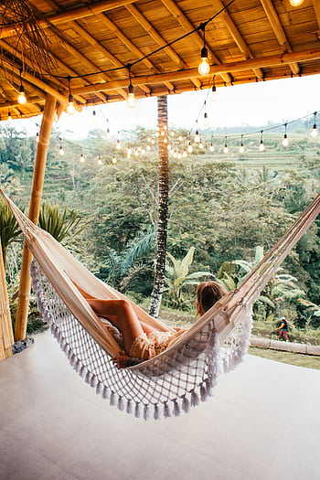Woman lounging in a hammock on a serene tropical veranda surrounded by nature. HD phone wallpaper