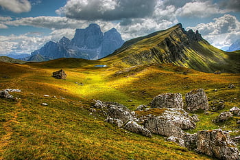 Explore a stunning alpine landscape with rolling hills and majestic mountains under a cloudy sky. HD wallpaper