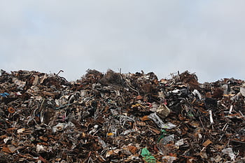 A large pile of scrap metal and waste at a landfill against a cloudy sky. HD wallpaper