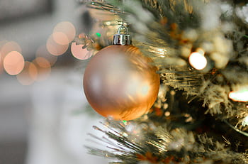 Close-up of a golden Christmas ornament hanging on a beautifully decorated tree with blurred festive lights. HD wallpaper