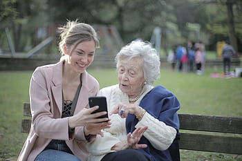 A joyful moment between a young woman and an elderly lady using a smart in the park. HD wallpaper