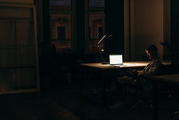 A man working late at night in a dimly lit office, with a bright laptop screen. HD wallpaper