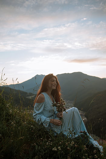 A woman in a blue dress sits on a grassy hill, enjoying the mountain sunset. HD phone wallpaper