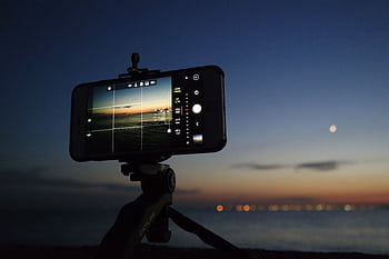An evening scene of a smart on a tripod taking a of the sunset over the ocean. HD wallpaper