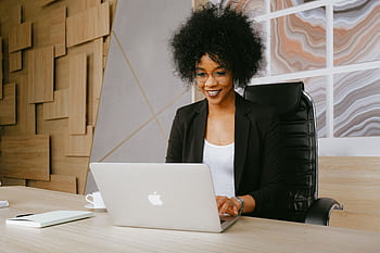 Smiling woman working remotely on a laptop in a stylish office setting. HD wallpaper