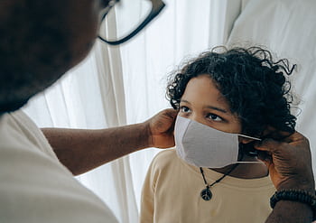 An adult assists a child in wearing a protective face mask indoors for safety. HD wallpaper