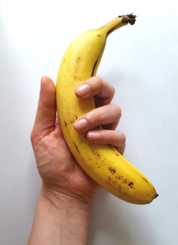 Close-up of a hand holding a ripe yellow banana against a white backdrop, showcasing freshness and tropical vibes. HD phone wallpaper