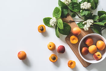 A bright still life of fresh apricots and blossoms on a cutting board, perfect for healthy eating. HD wallpaper
