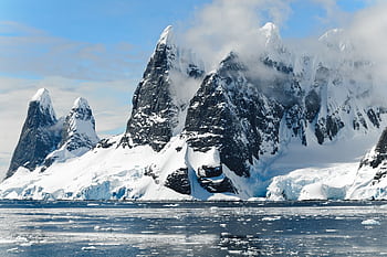 Majestic snowy peaks rise over icy Antarctic waters, showcasing untouched nature. HD wallpaper