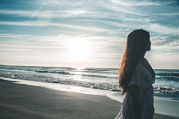 Silhouette of a woman strolling along a tranquil beach during sunset, embracing nature's beauty. HD wallpaper