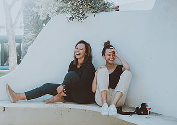 Two women laughing together outdoors, enjoying leisure time and friendship. HD wallpaper