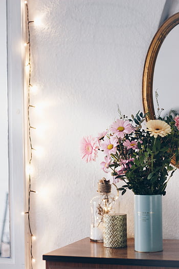 A cozy interior featuring a floral arrangement in a vase, with string lights and a mirror creating a warm atmosphere. HD phone wallpaper