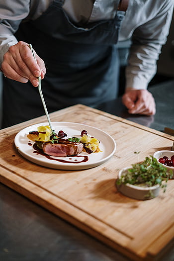 Chef meticulously plates a gourmet dish on a wooden board in a professional kitchen setting. HD phone wallpaper